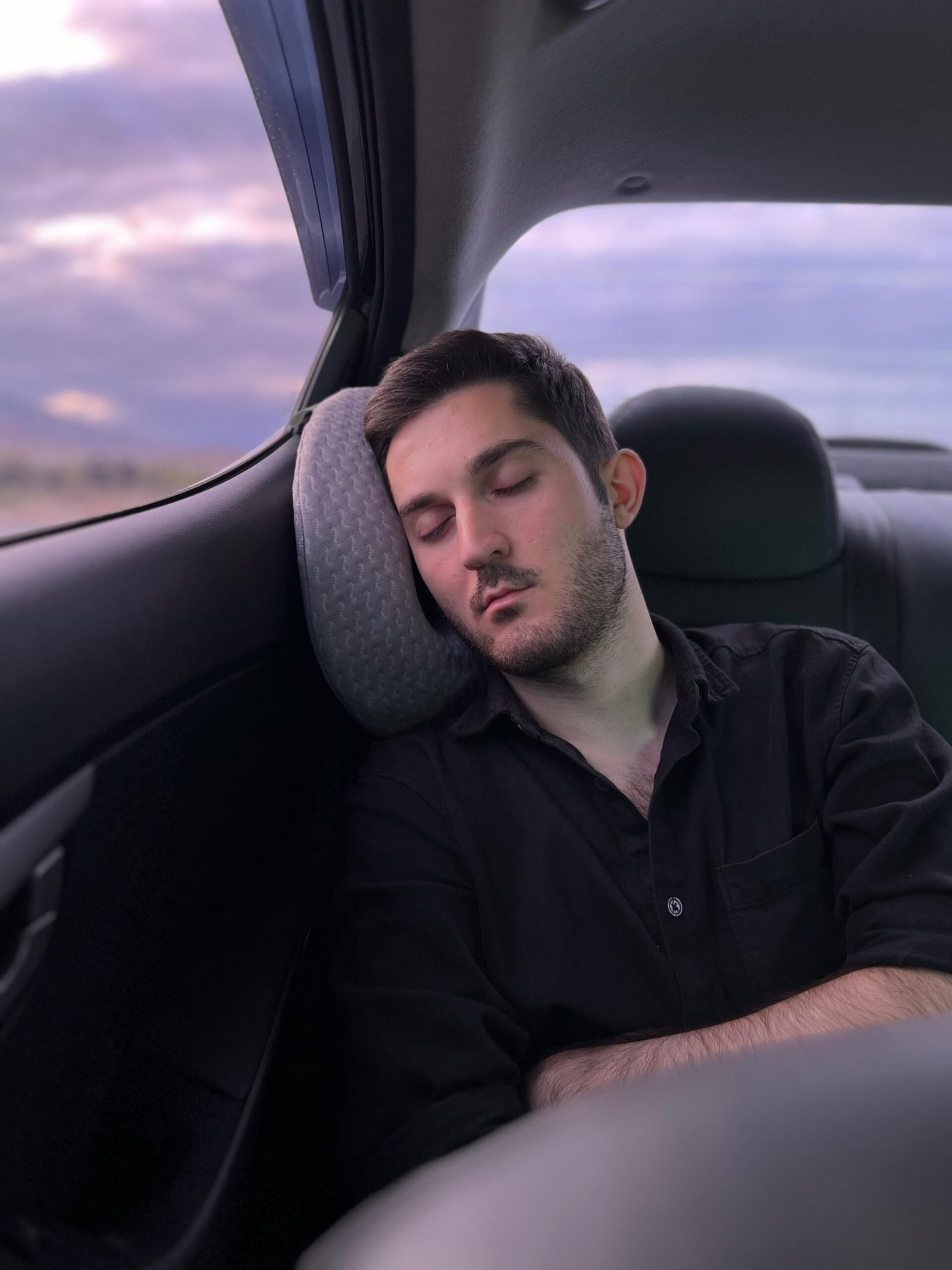 Young man in black shirt sleeping in backseat of a car during twilight in Sijazan, Azerbaijan.